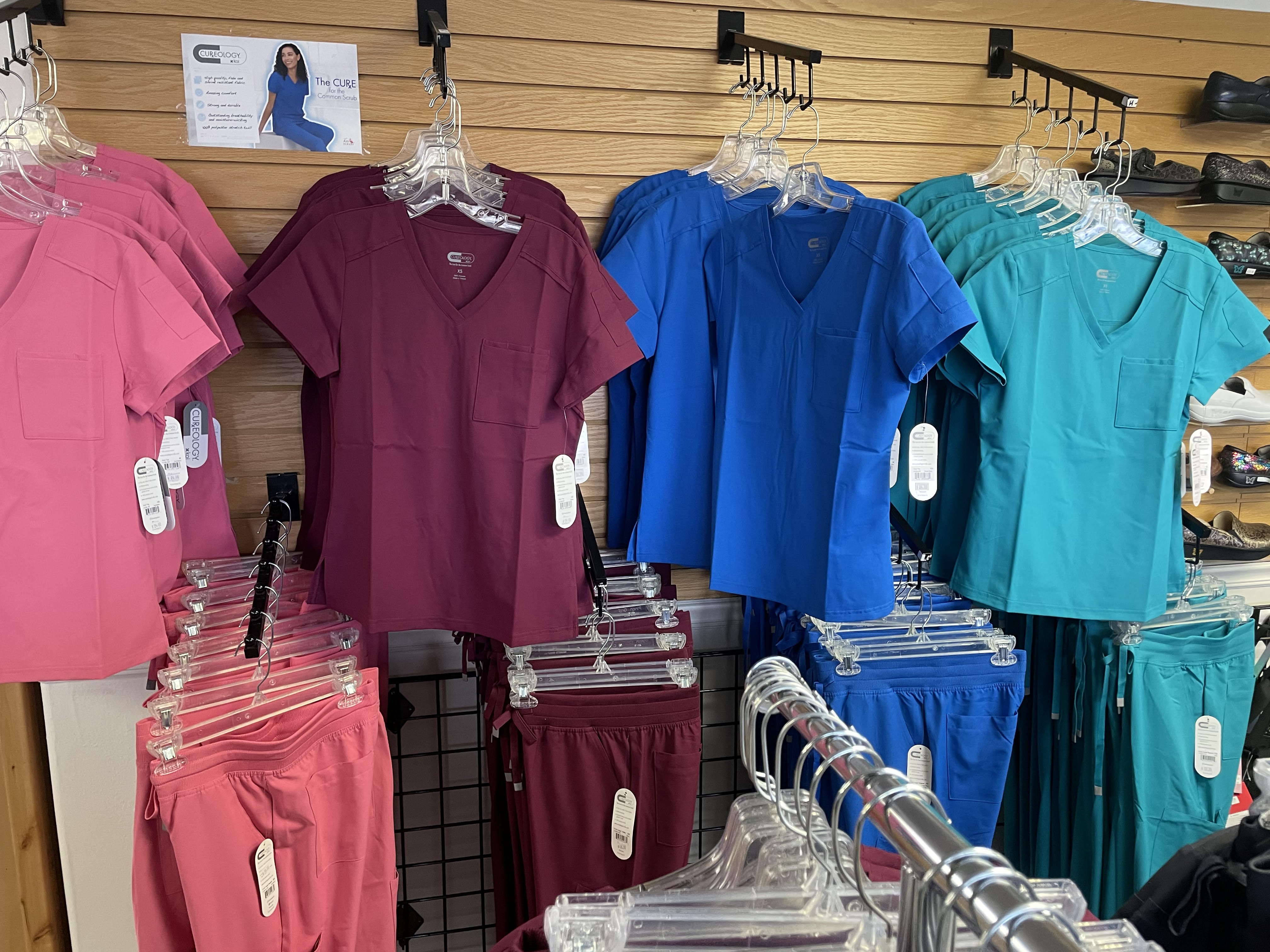 Cureology scrub tops in pink, burgundy, royal blue, and teal on display