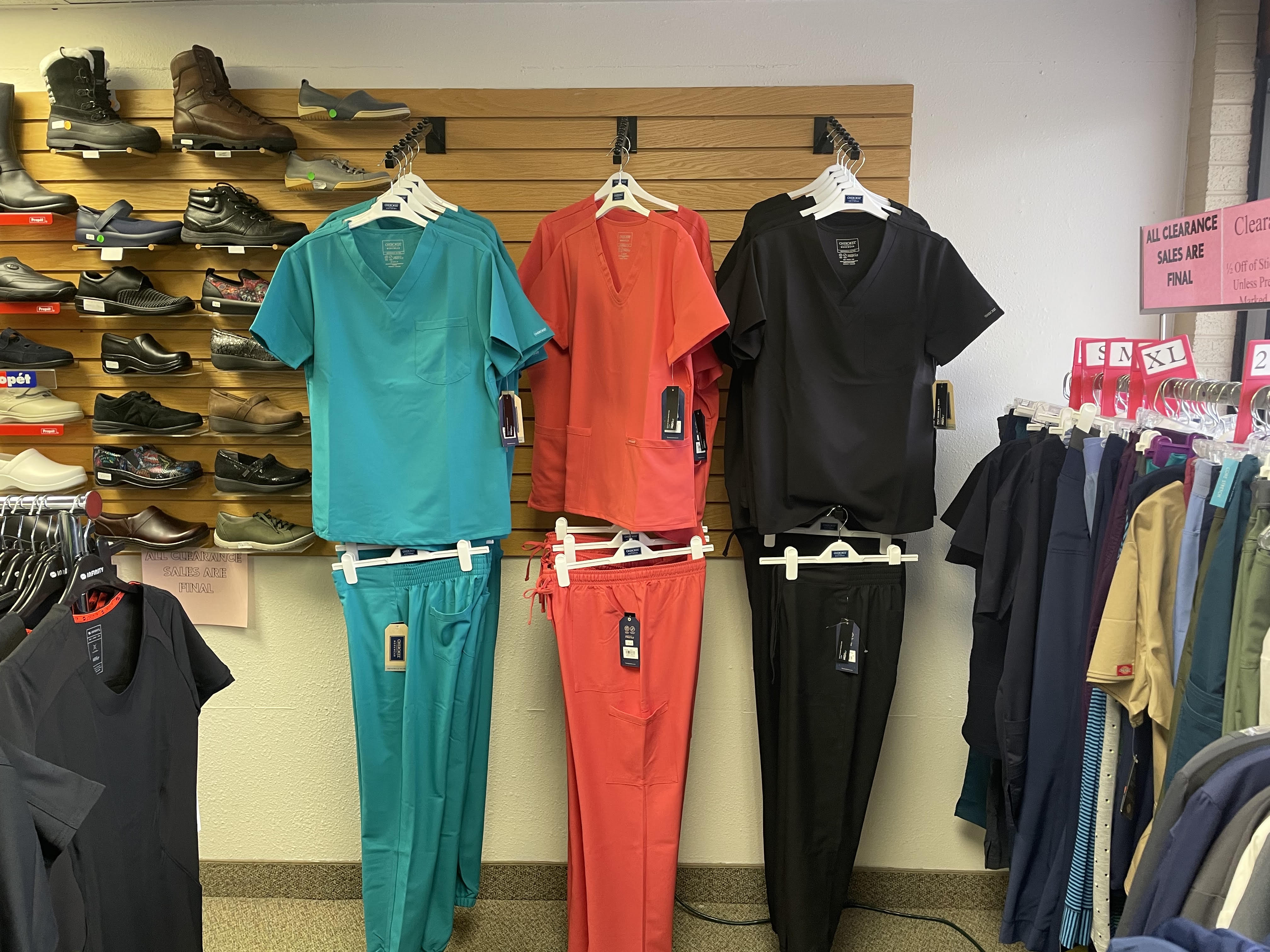 Coordinated teal, coral, and black scrub sets displayed beneath a footwear wall